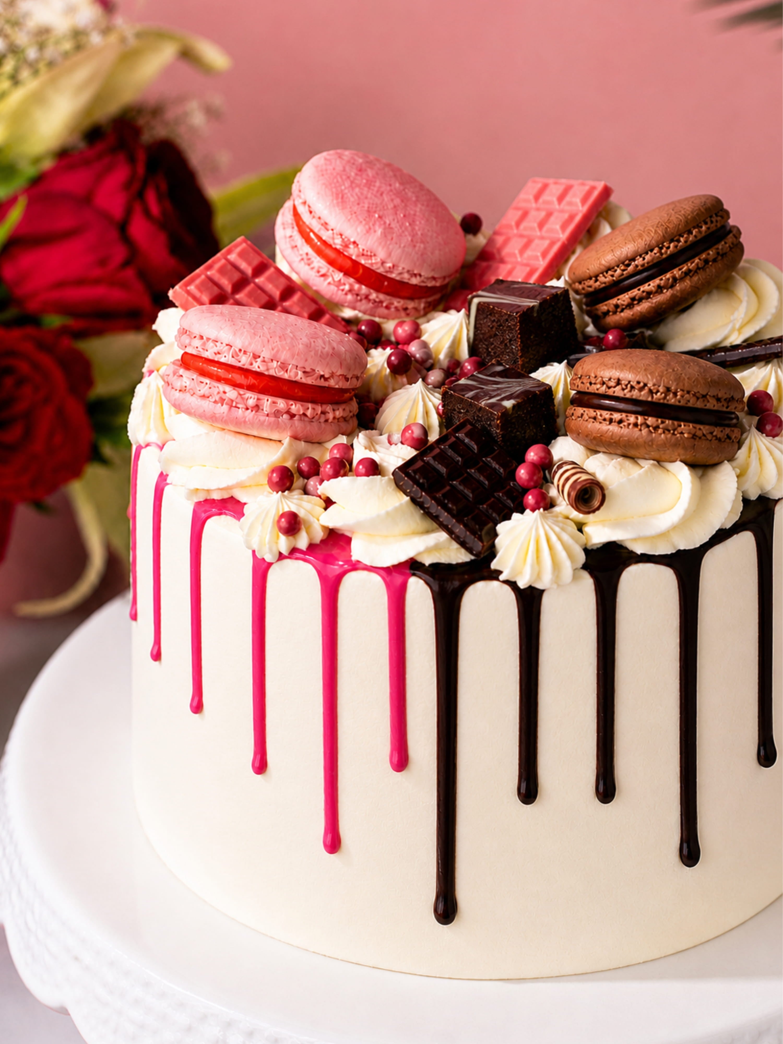 Decorative cake with macarons, chocolate bars, and berries on a pink background