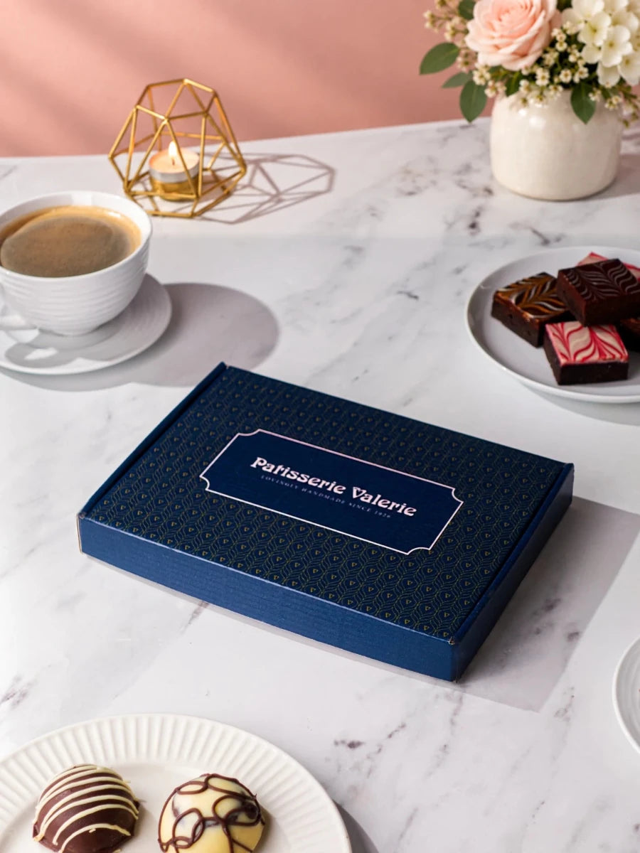 Closed Patisserie Valerie gift box with brownies and chocolate-coated cake bites on plates
