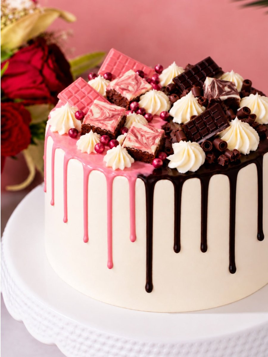 Close up of the Half and Half Drip Cake topping with pink chocolate bars, marbled brownie bites and pink pearls on one side and dark chocolate bars and curls on the other