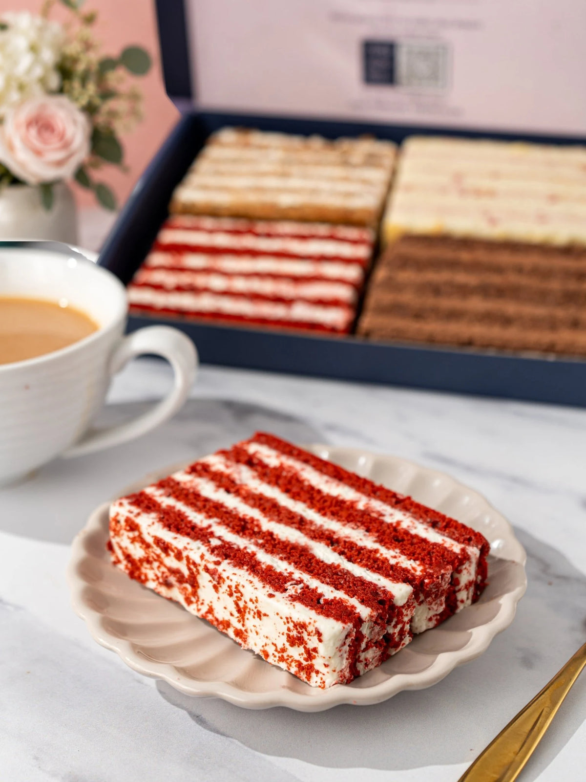 Red velvet cake slices on a white plate with the Favourites Quartet gift box behind by Patisserie Valerie