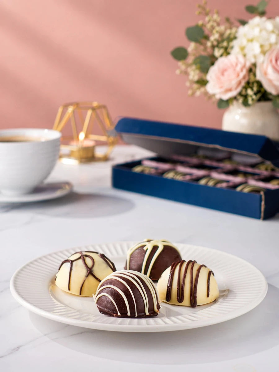 Four chocolate-coated cake bites on a plate with the open gift box behind by Patisserie Valerie