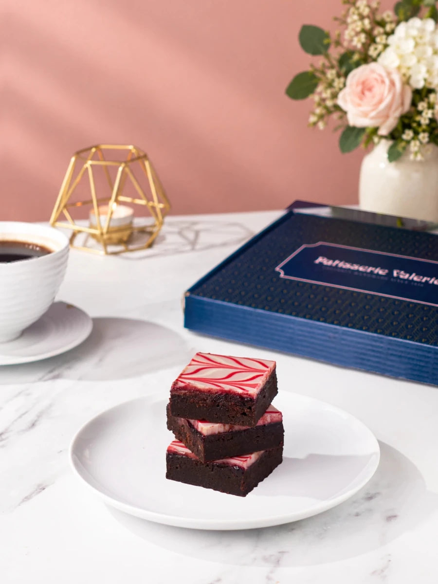 Chocolate brownies with pink icing stacked on a plate beside the birthday gift box by Patisserie Valerie