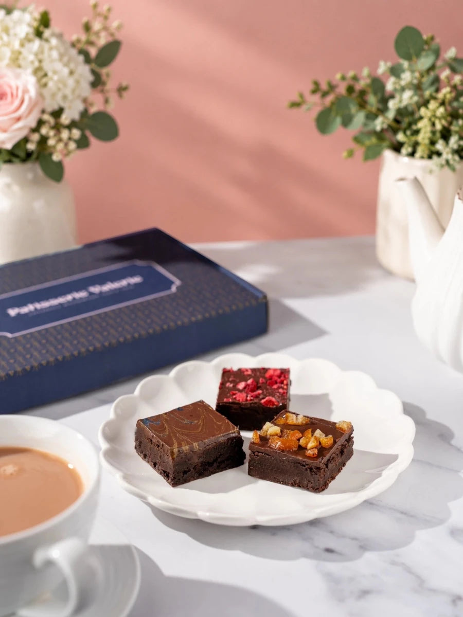 Three assorted Kind Bakes vegan brownies on a white plate beside the gift box by Patisserie Valerie