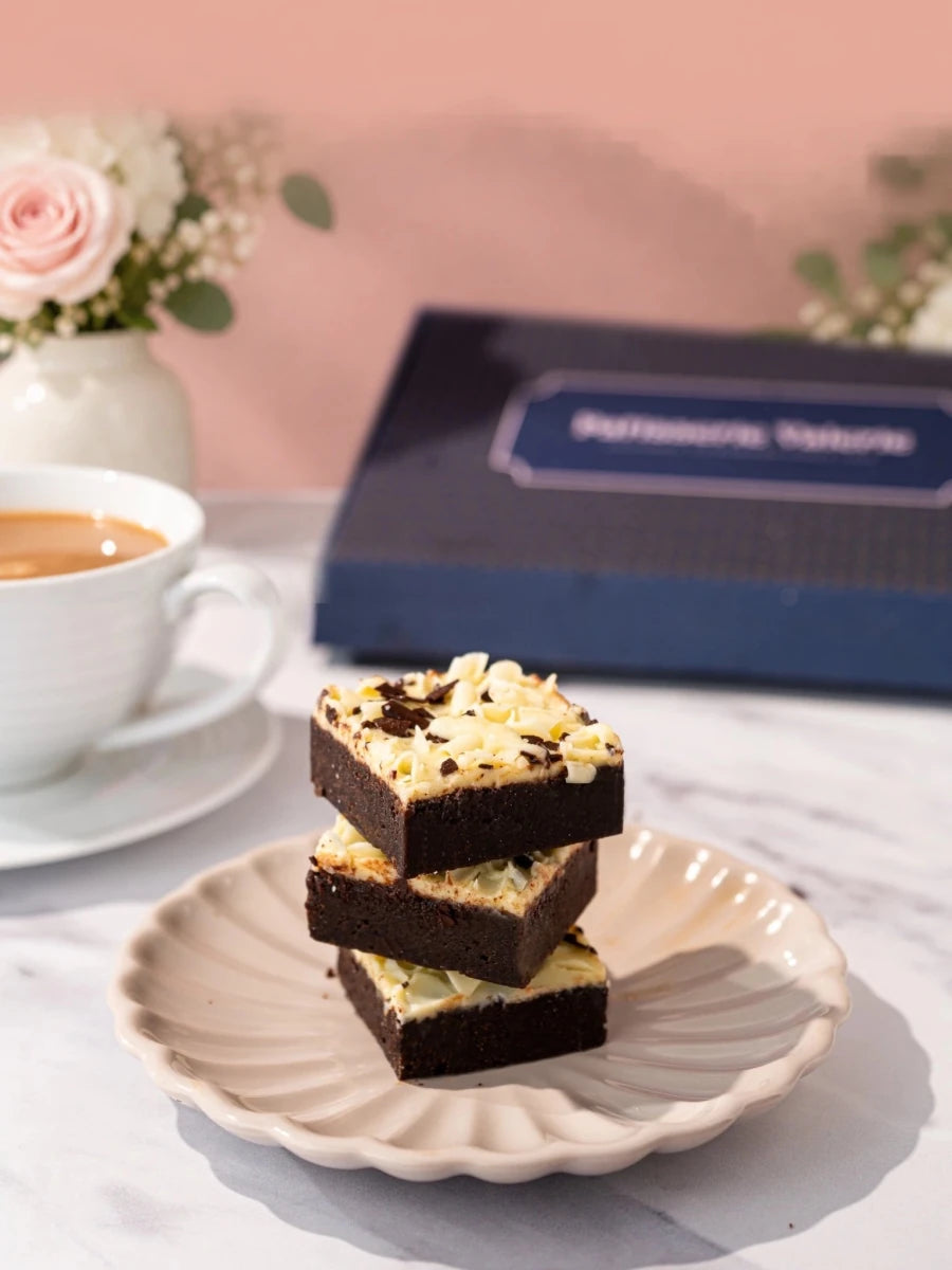 Luxury brownies topped with chocolate curls stacked on a white plate by Patisserie Valerie