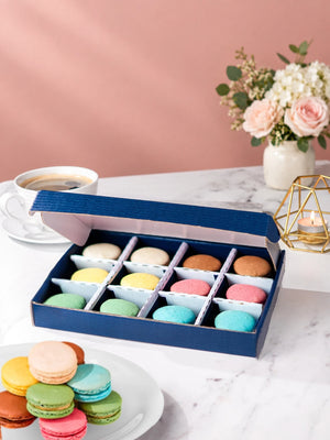 Open gift box of 12 mixed macarons with a selection on a plate by Patisserie Valerie