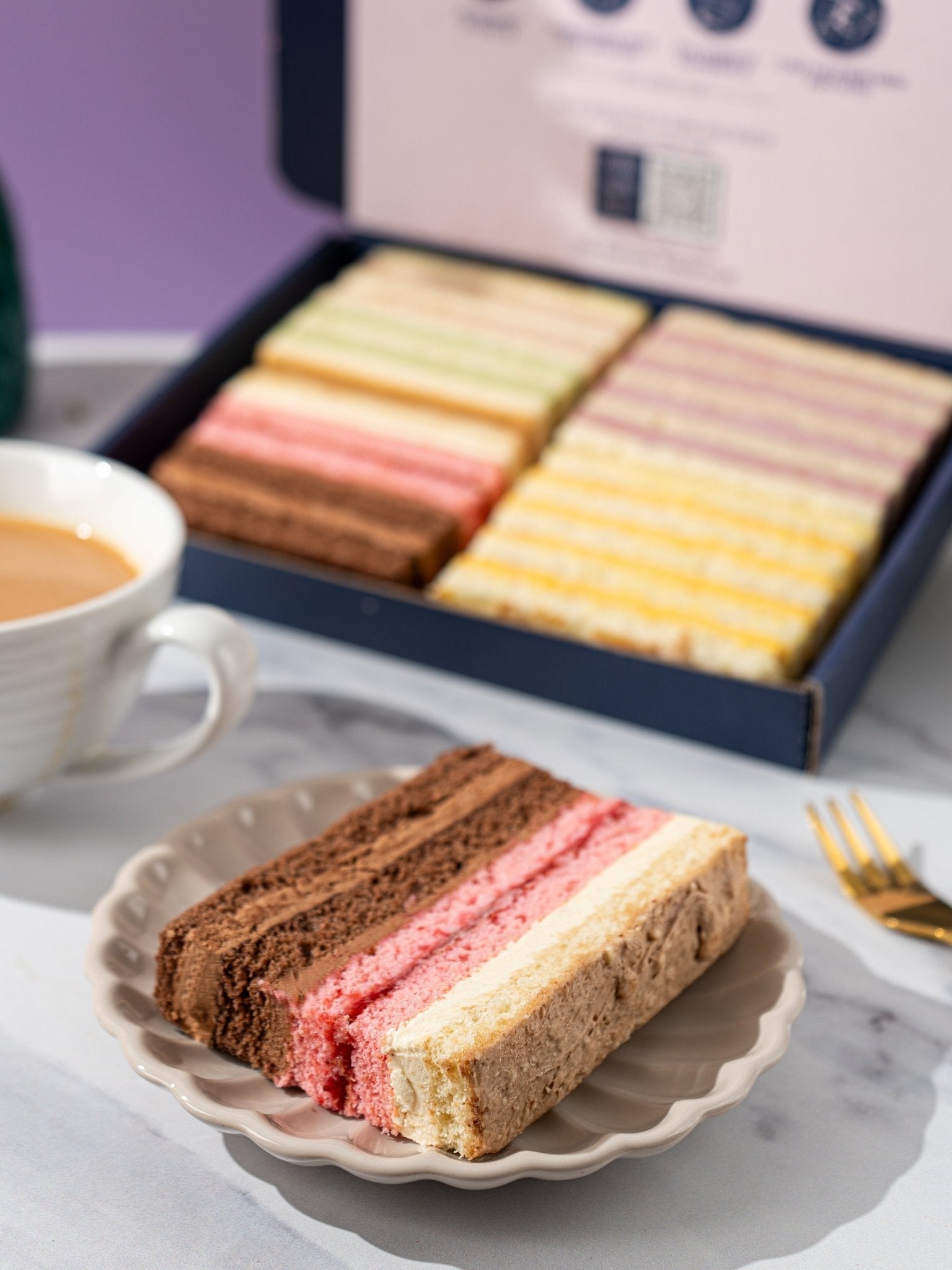 Patisserie Valerie's handmade Summer Favourites Cake Gift Box opened to reveal layered sponge slices, one served with tea